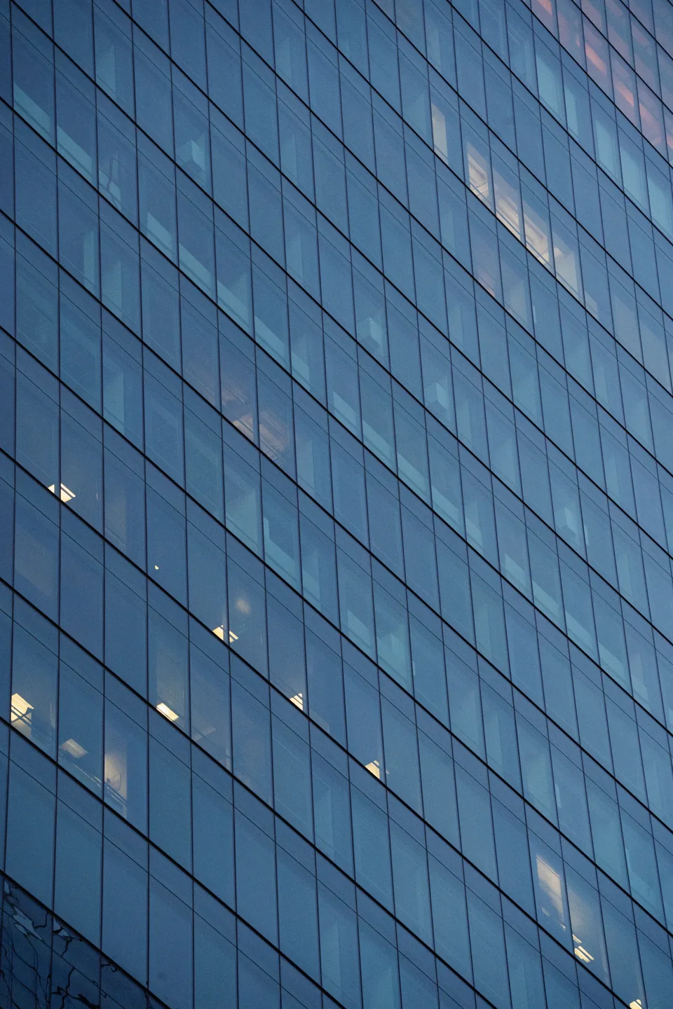Illustrative photograph: Blue glazed office facade in a regular grid, with some interior lights visible