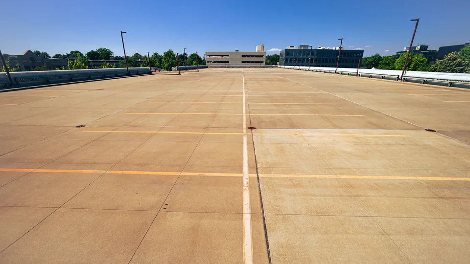 Illustrative photograph: Open concrete parking deck with painted bay markings and lamp posts